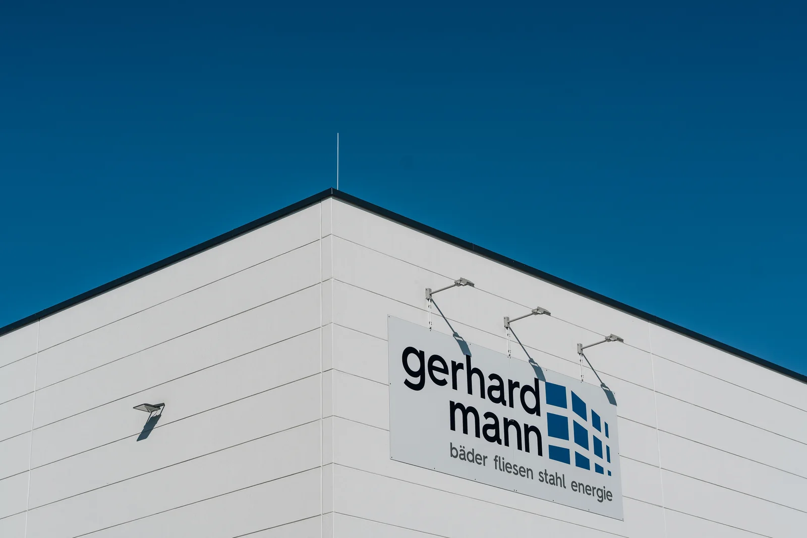 Gerhard-Mann-Schild an der weißen Hallenfassade vor blauem Himmel