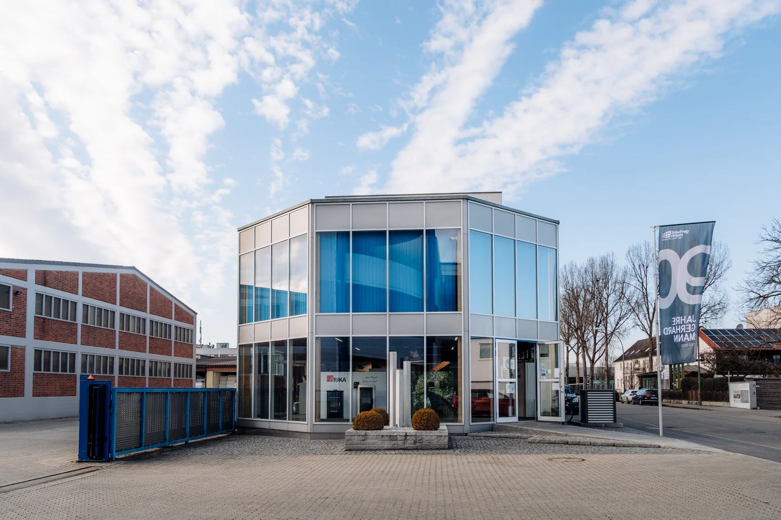 Energiekompetenzzentrum von Gerhard Mann: zweigeschossiger Glasbau mit blauen Vorhängen neben dem blauen Hoftor