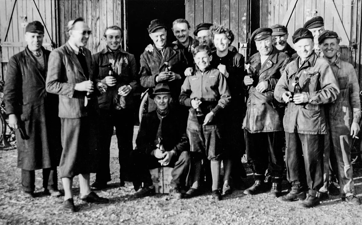 Historische Aufnahme: Mitarbeiter in Arbeitskleidung vor einem Holztor